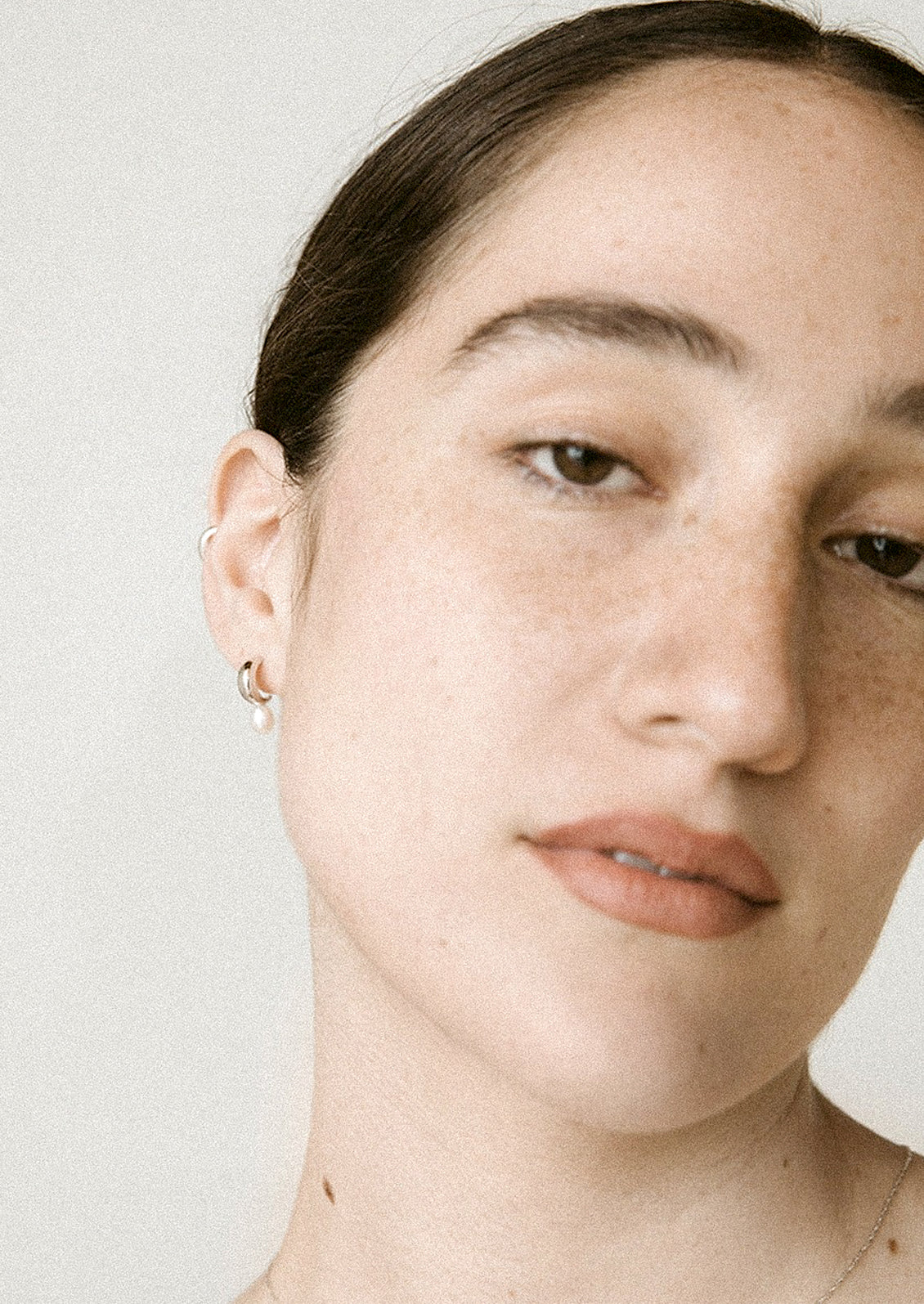 A pair of silver hoop earrings with attached pearl.