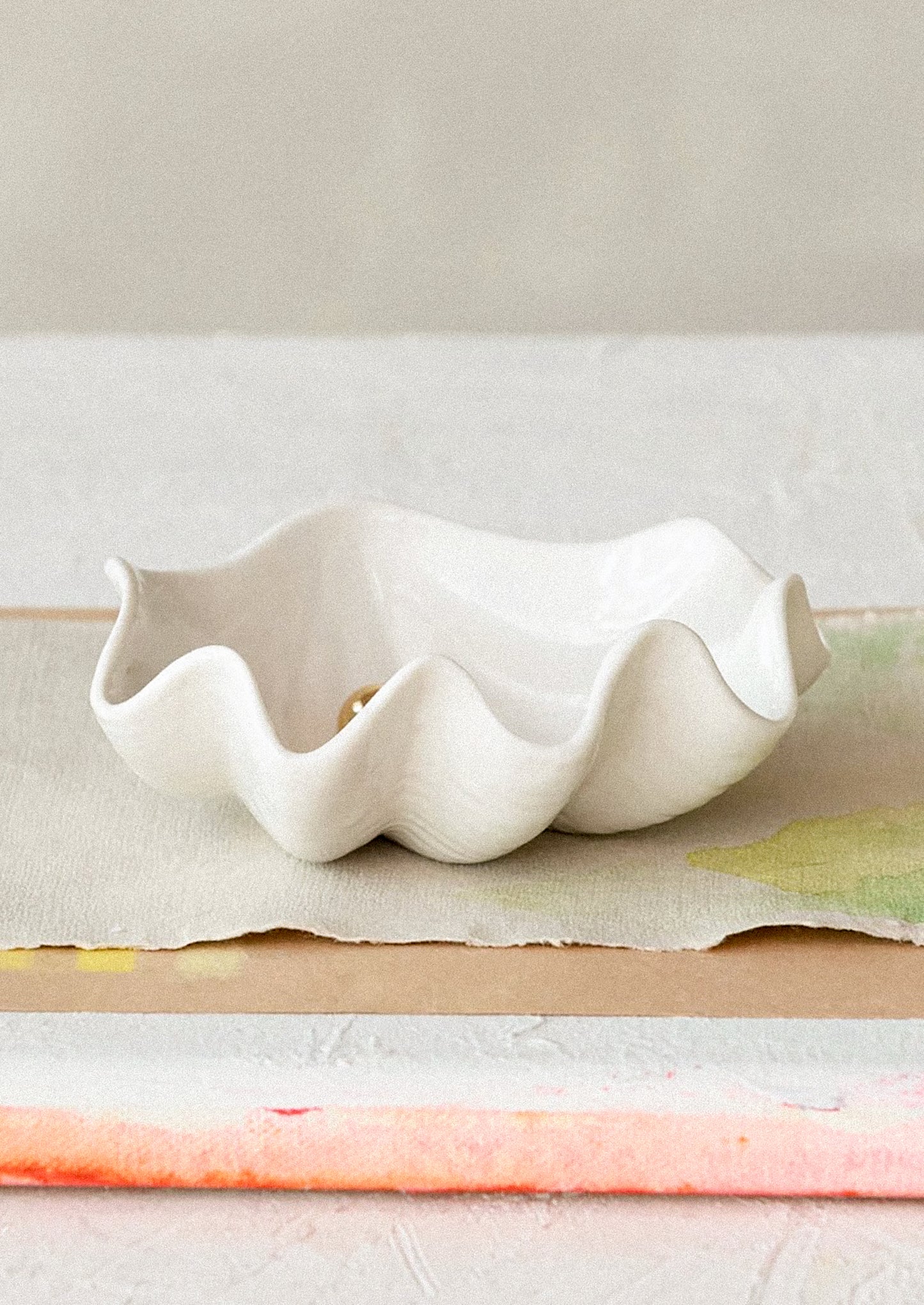 An oyster shaped ceramic bowl in white with gold pearl detail at center.