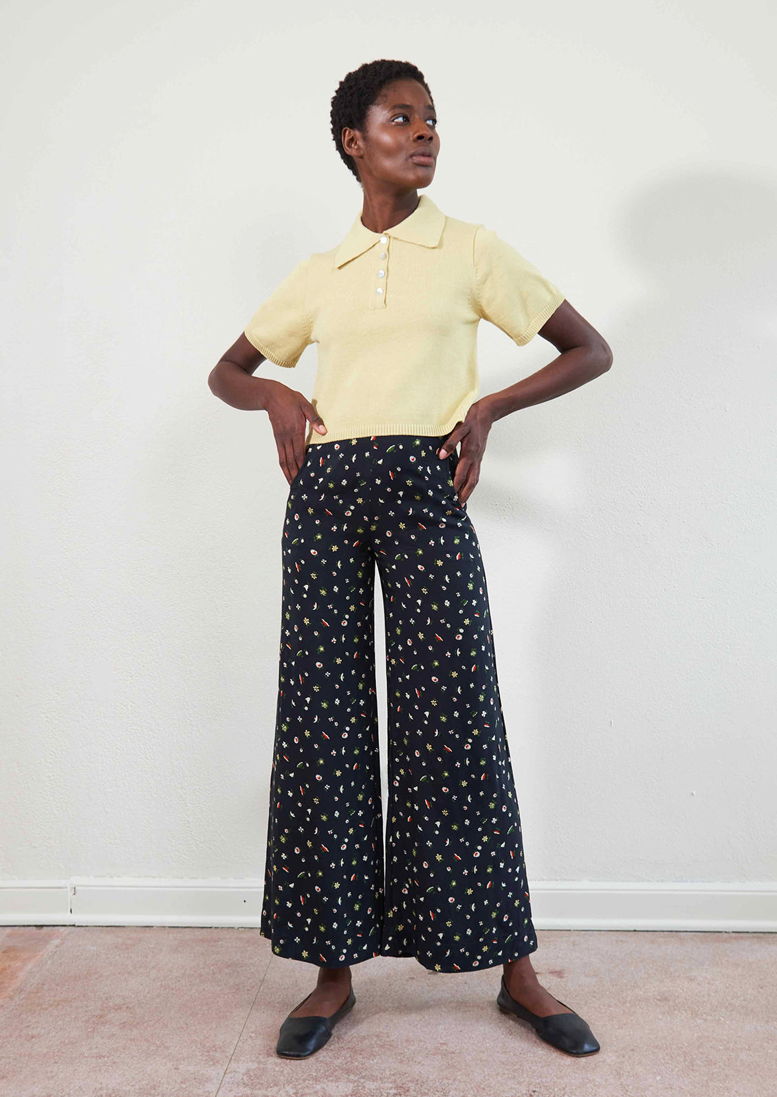 A woman wearing a pair of high waisted pants in black with multicolor botanical print throughout.