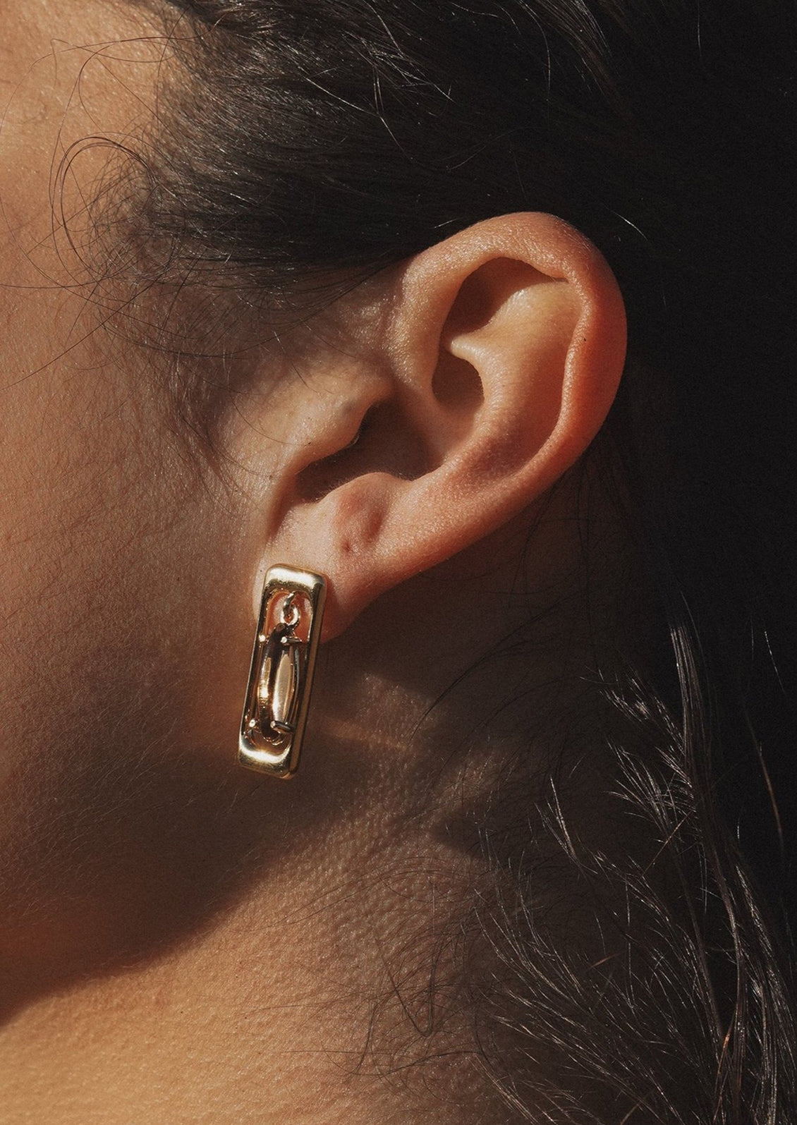 A pair of gold earrings in rectangular shape with pendulum brown baguette-cut gemstone at center.
