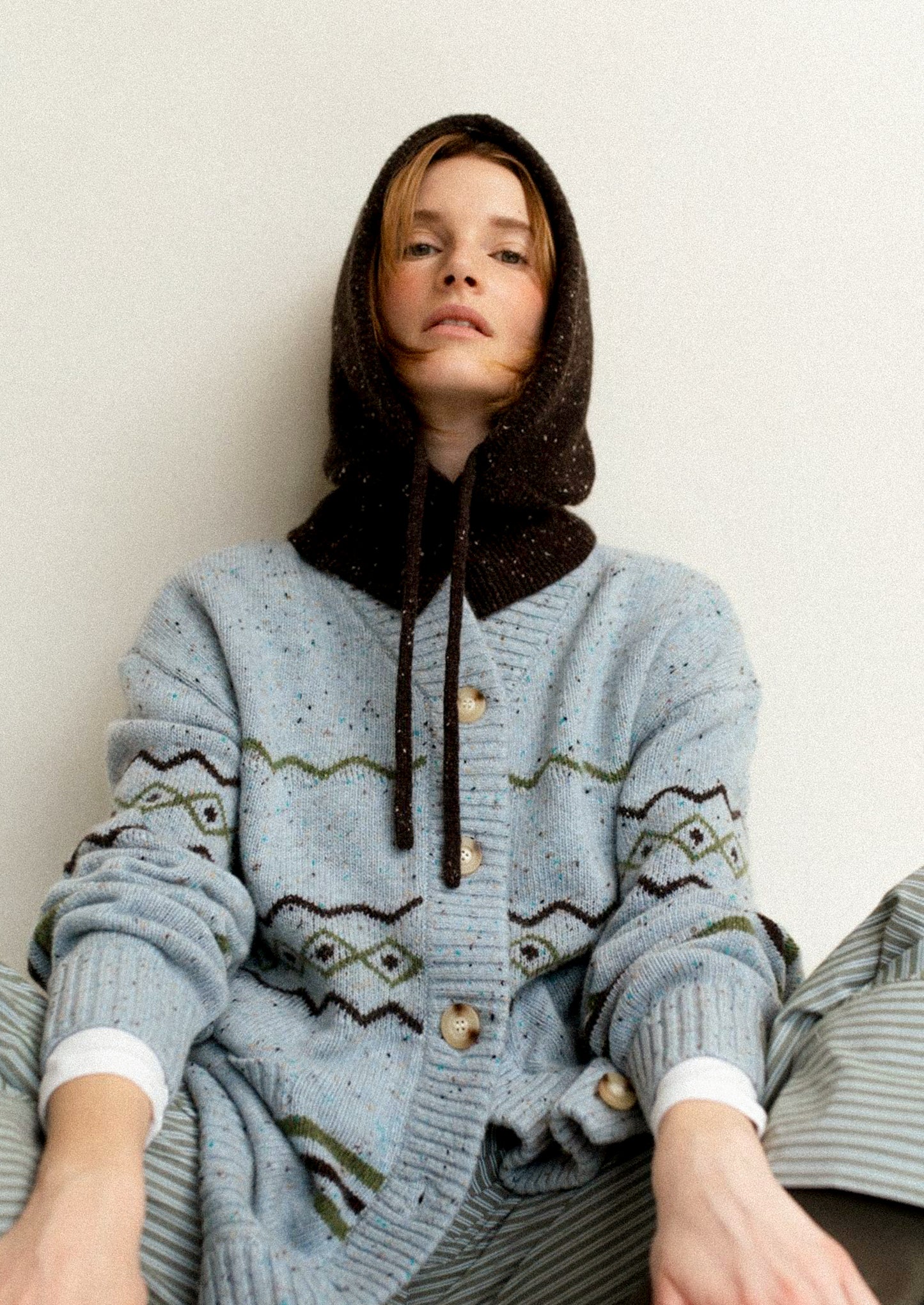 Person wearing a blue patterned cardigan with a hood against a plain background