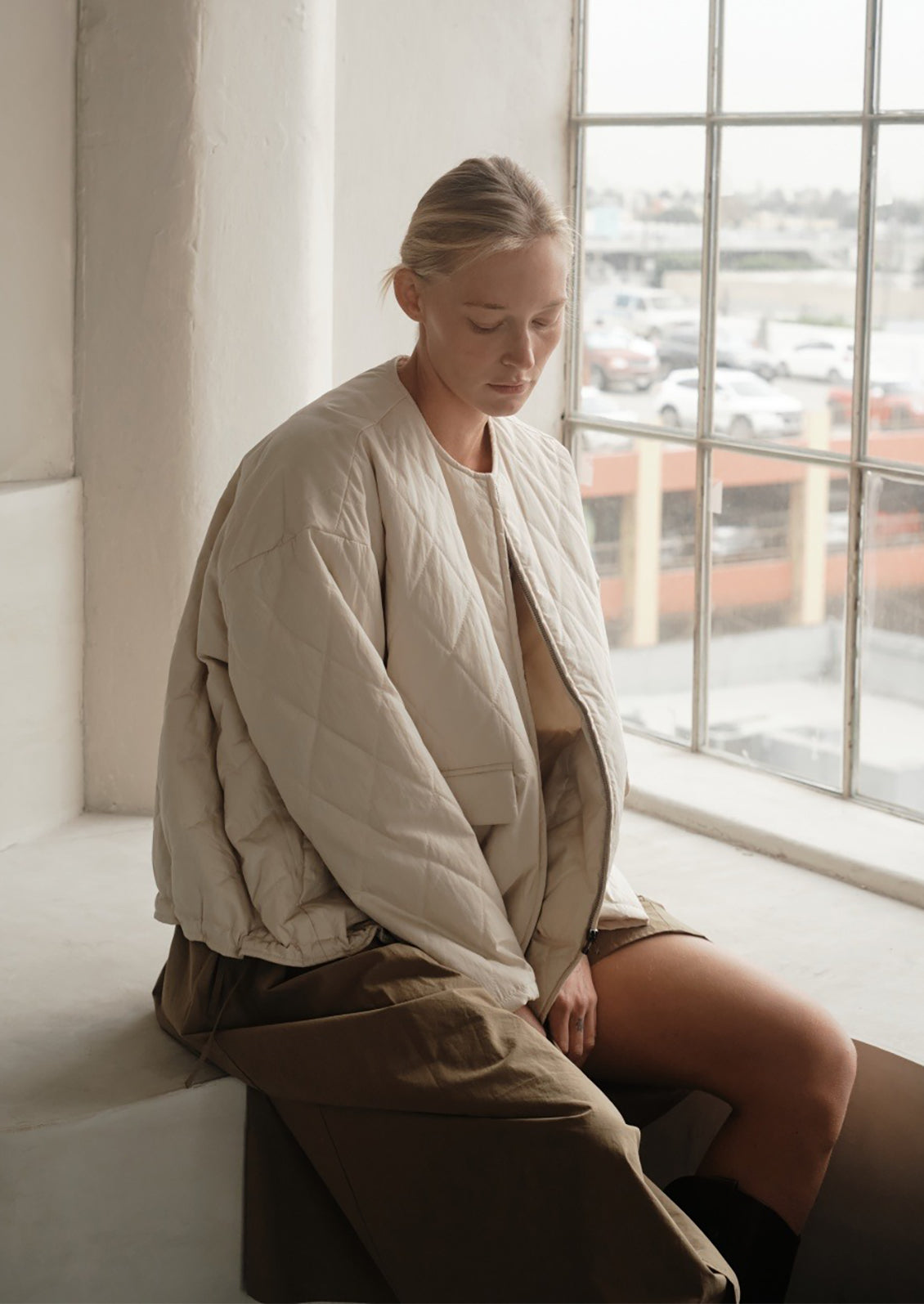 A woman wearing a padded quilted jacket with bottom drawstring detail in cream.