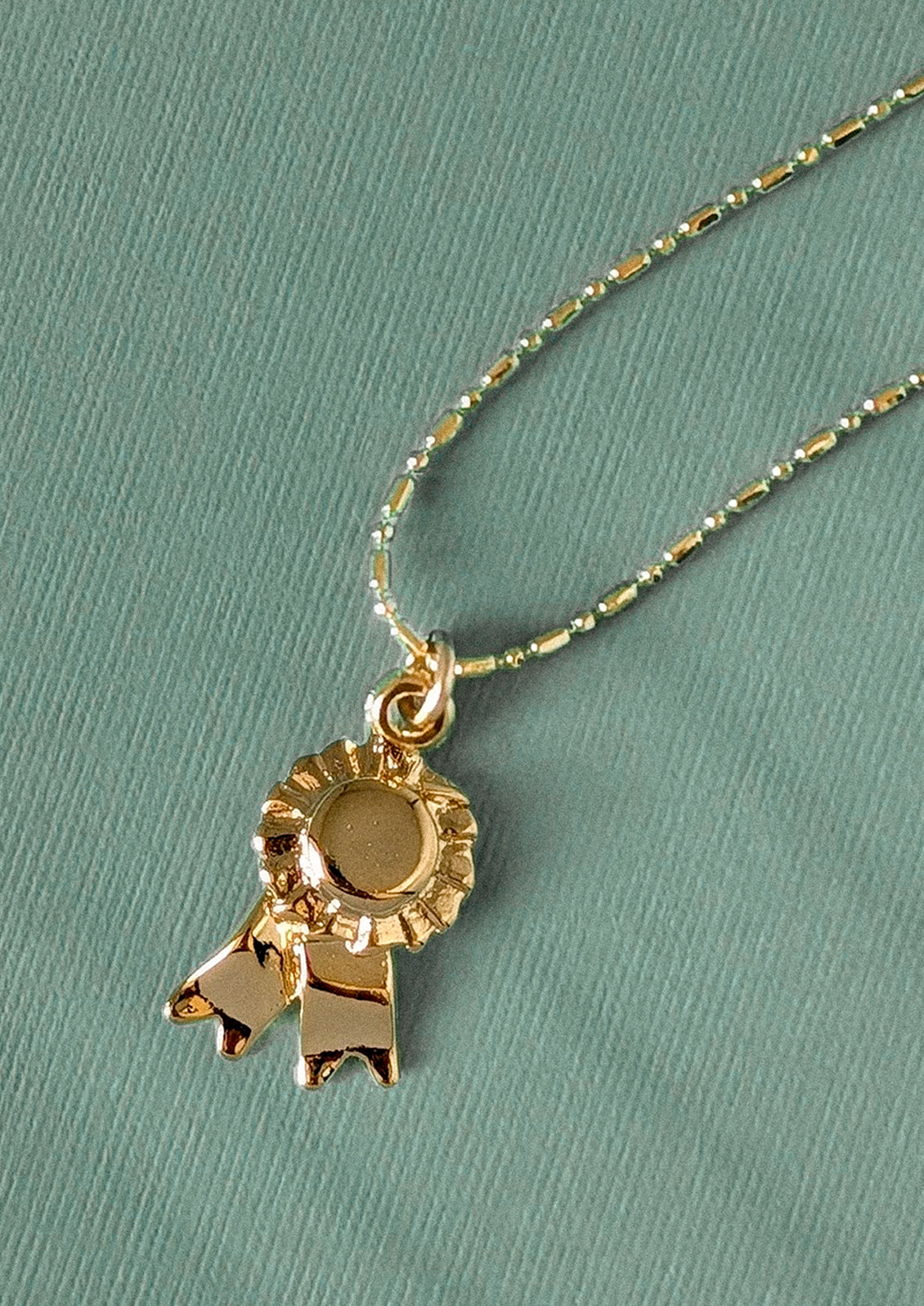 Gold necklace with a ribbon charm on a teal background