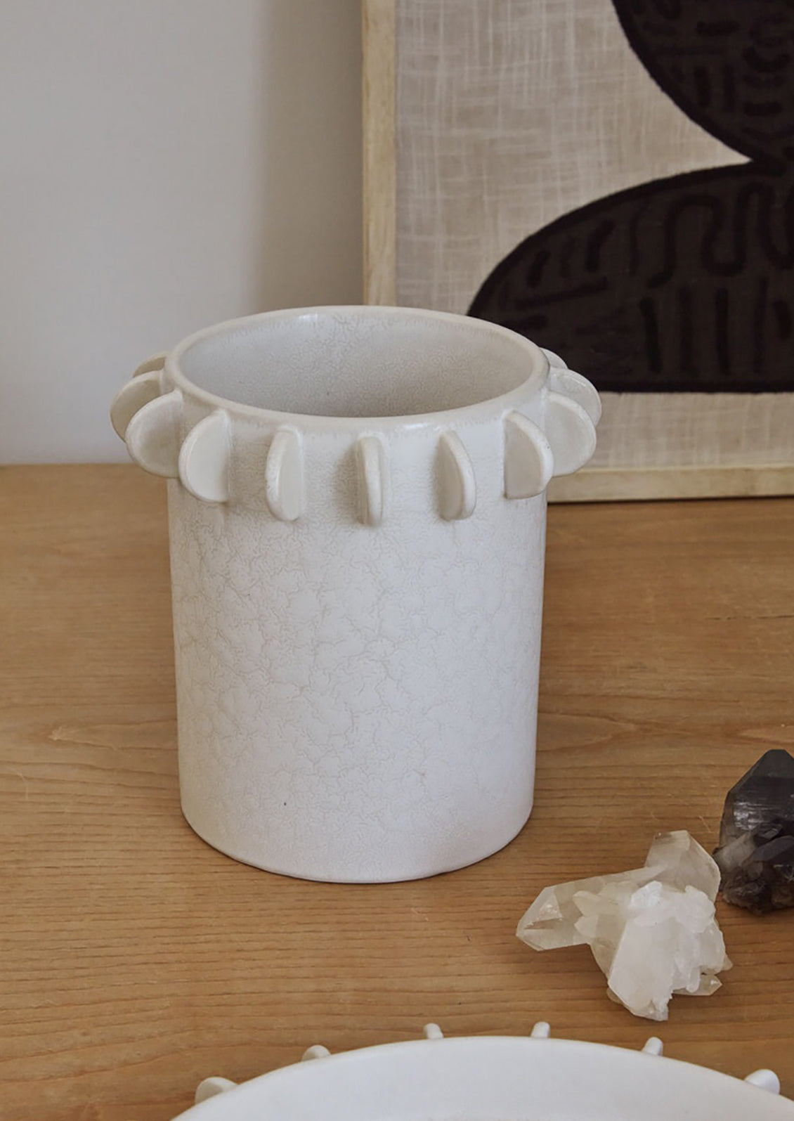 A white ceramic cylindrical crock with decorative tab detail around top rim.