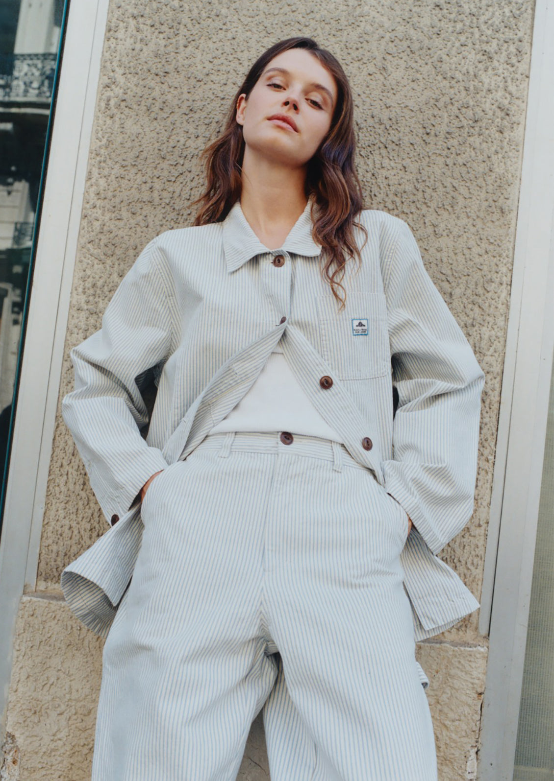 Woman wearing a light gray outfit with a textured wall background