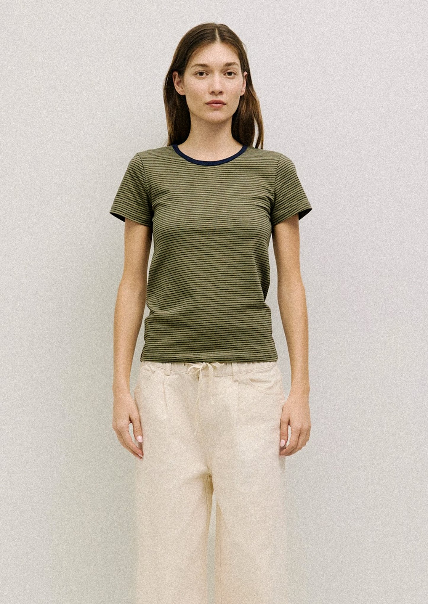 A person wearing a striped t-shirt in olive green with navy stripes and neckline.