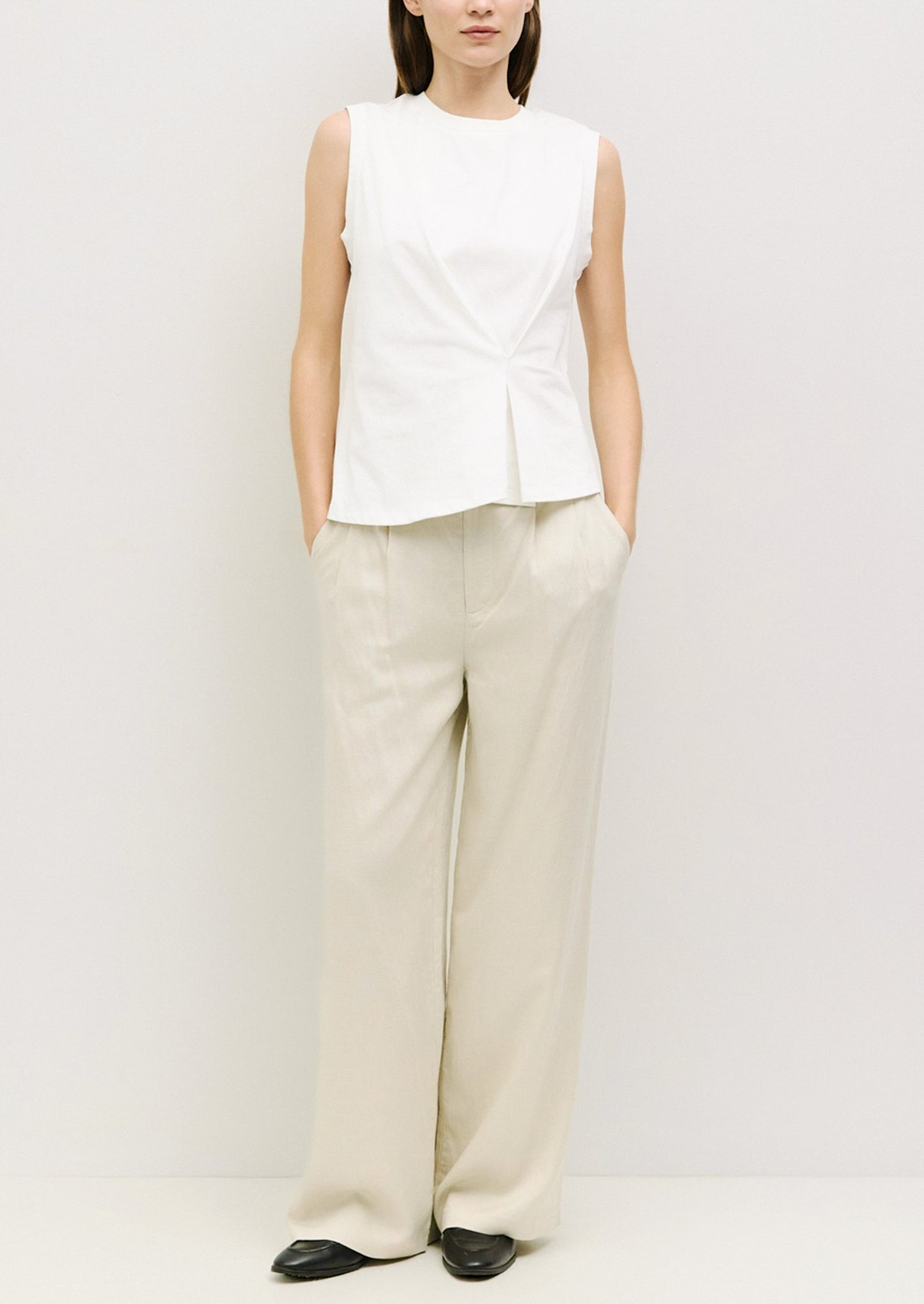 A woman wearing a sleeveless tee in white with drape tuck detail at front.