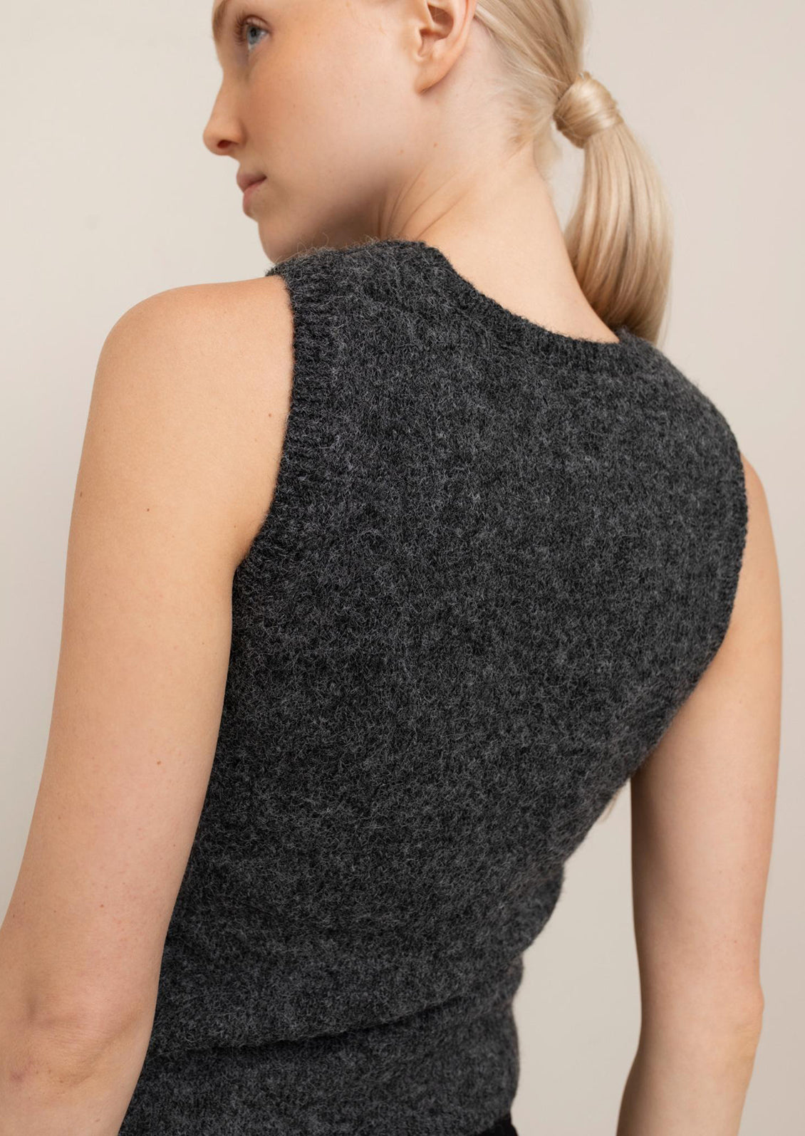 Person wearing a dark gray sleeveless knitted top against a neutral background