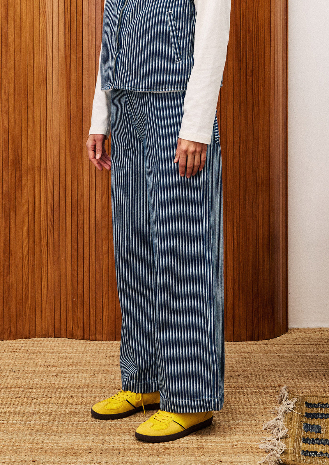 Person wearing a blue striped outfit with yellow shoes in front of a wooden panel.