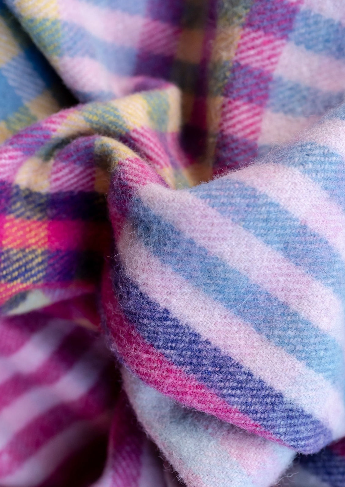 A colorful wool blanket with plaid pattern in pink, purple, yellow and blue hues.