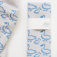 1: A grey linen tea towel with blue duck illustration print.