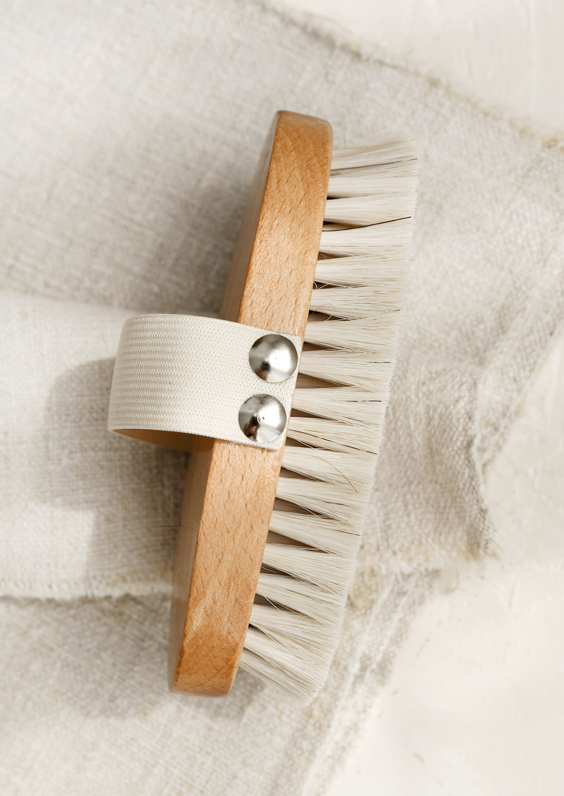 An oval shaped wood and bristle bath brush with elastic hand strap.