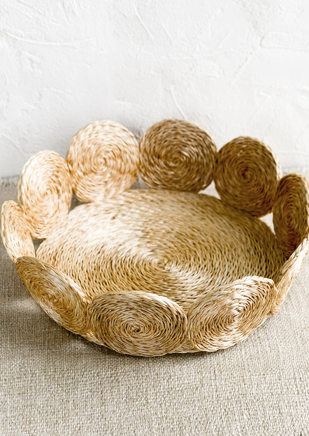 Natural / Small: A round, shallow basket with woven circular border design in natural.