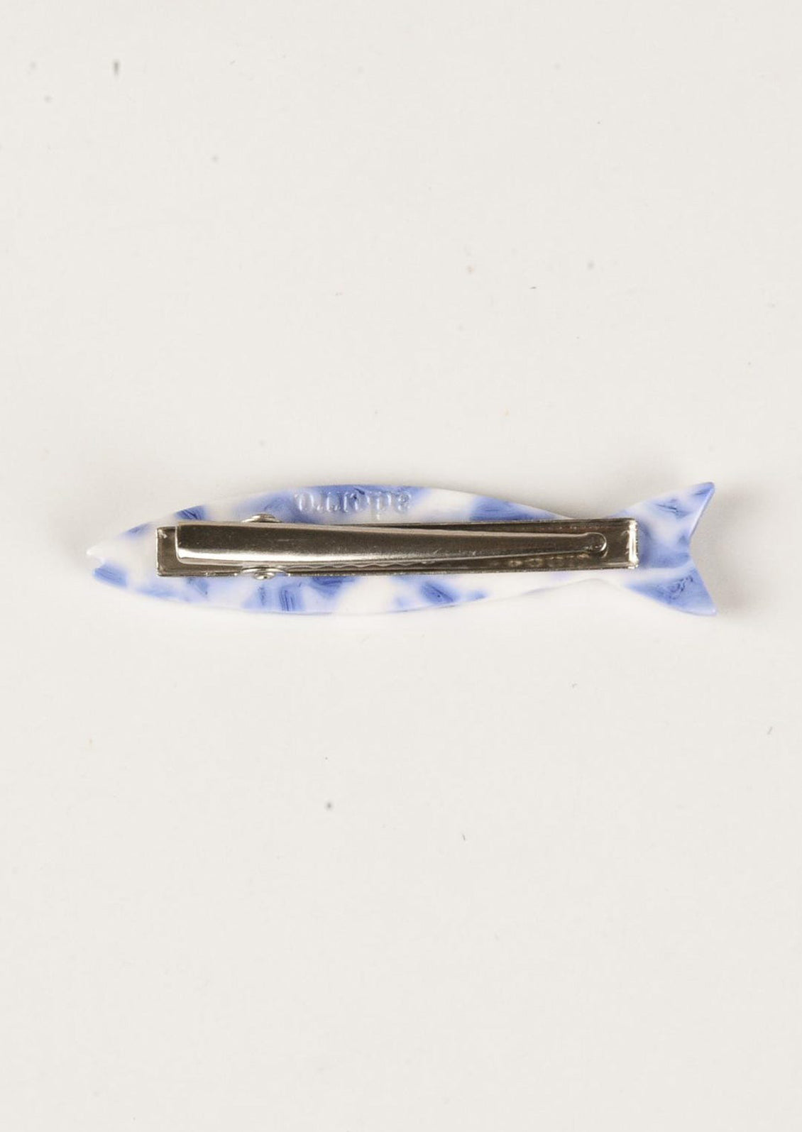 A blue and white barrette in the shape of a sardine with floral carved pattern.