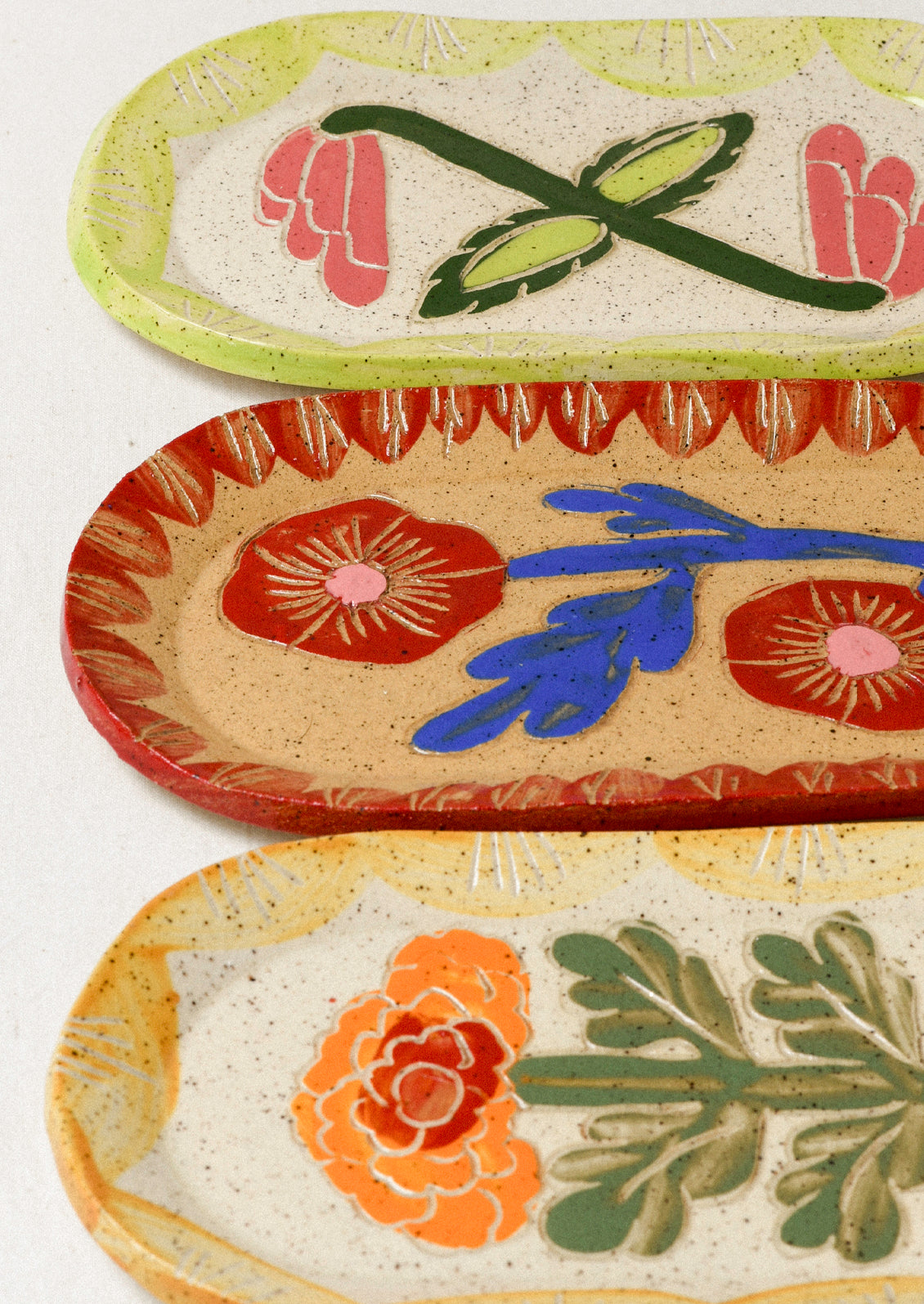 Three ceramic oval catchall trays each with an etched flower in the center and colorful border.