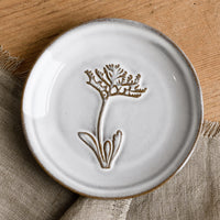 Dusty Miller: A grey glazed brown clay mini plate with raised flower design.