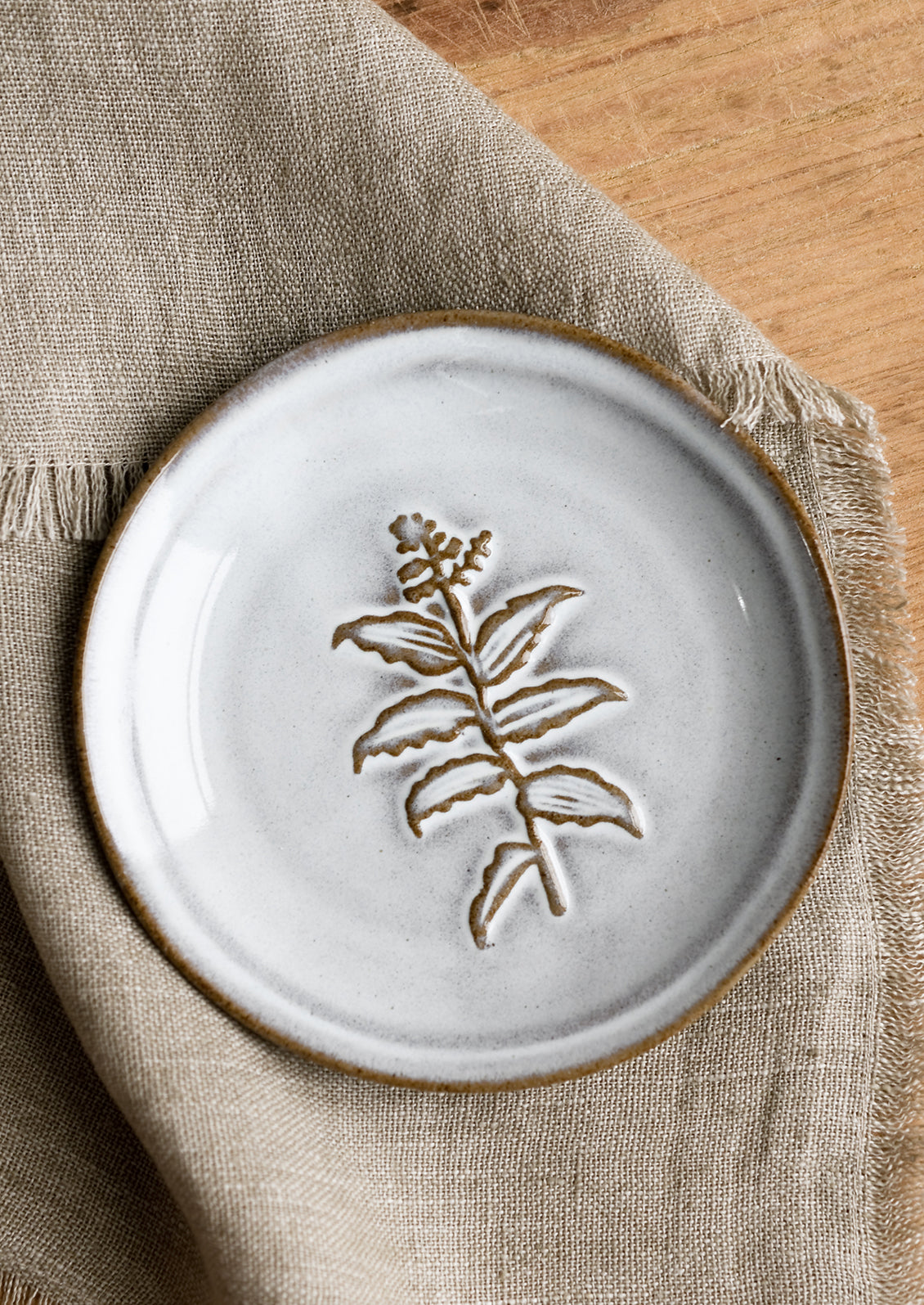 A grey glazed brown clay mini plate with raised flower design.
