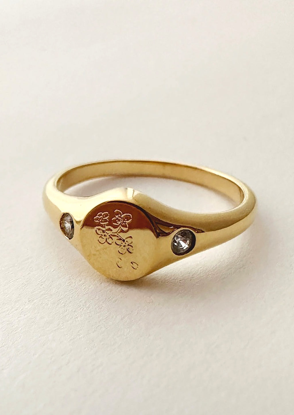 1: A gold signet ring with floral engraving with clear crystal on either side.