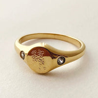 1: A gold signet ring with floral engraving with clear crystal on either side.