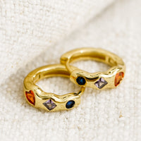 1: A pair of gold huggie hoop earrings with multicolor and multishape crystal detailing.