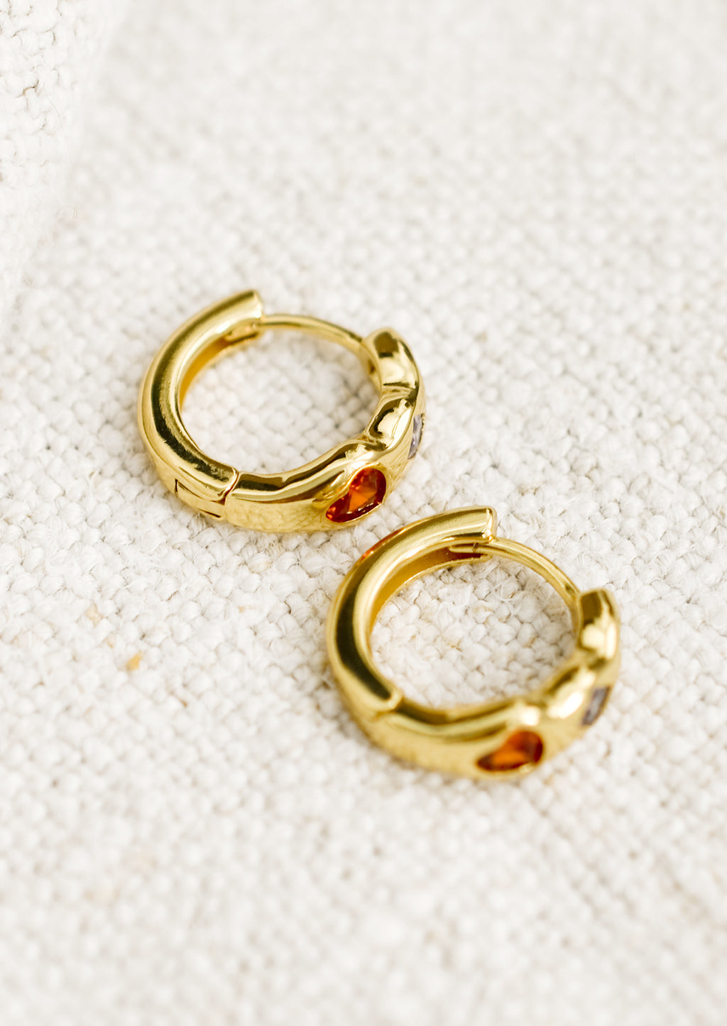 3: A pair of gold huggie hoop earrings with multicolor and multishape crystal detailing.