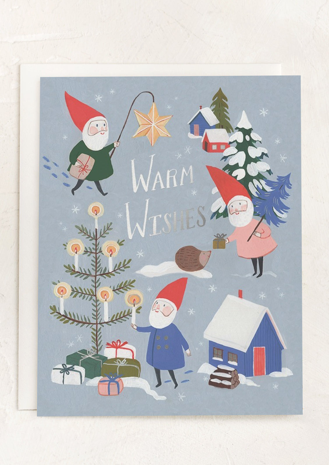 A blue card with illustration of gnomes doing Christmas activities, text reads Warm Wishes.