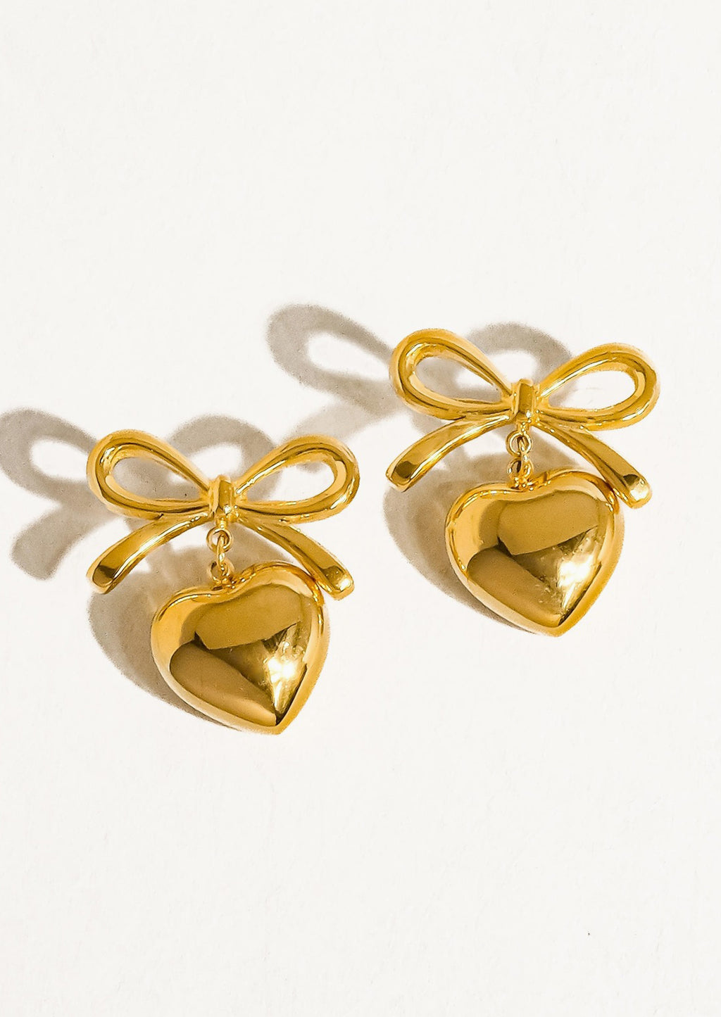 2: A pair of gold earrings with dangling heart charm and bow shaped post.