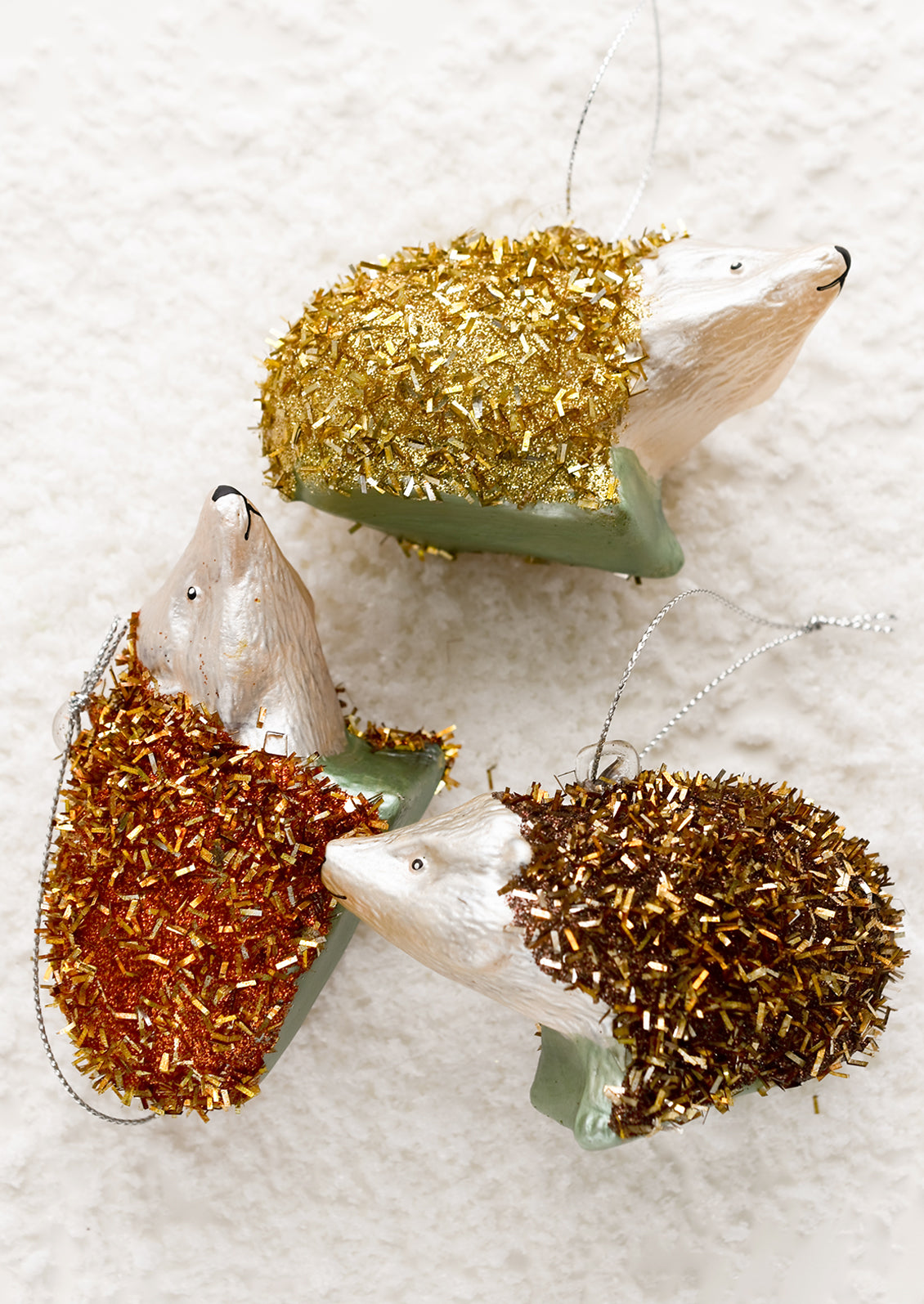 Holiday glass ornaments of hedgehogs in metallic tinsel.
