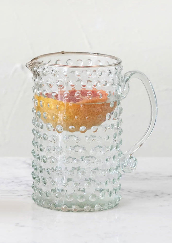 A clear glass pitcher with hobnail texture.