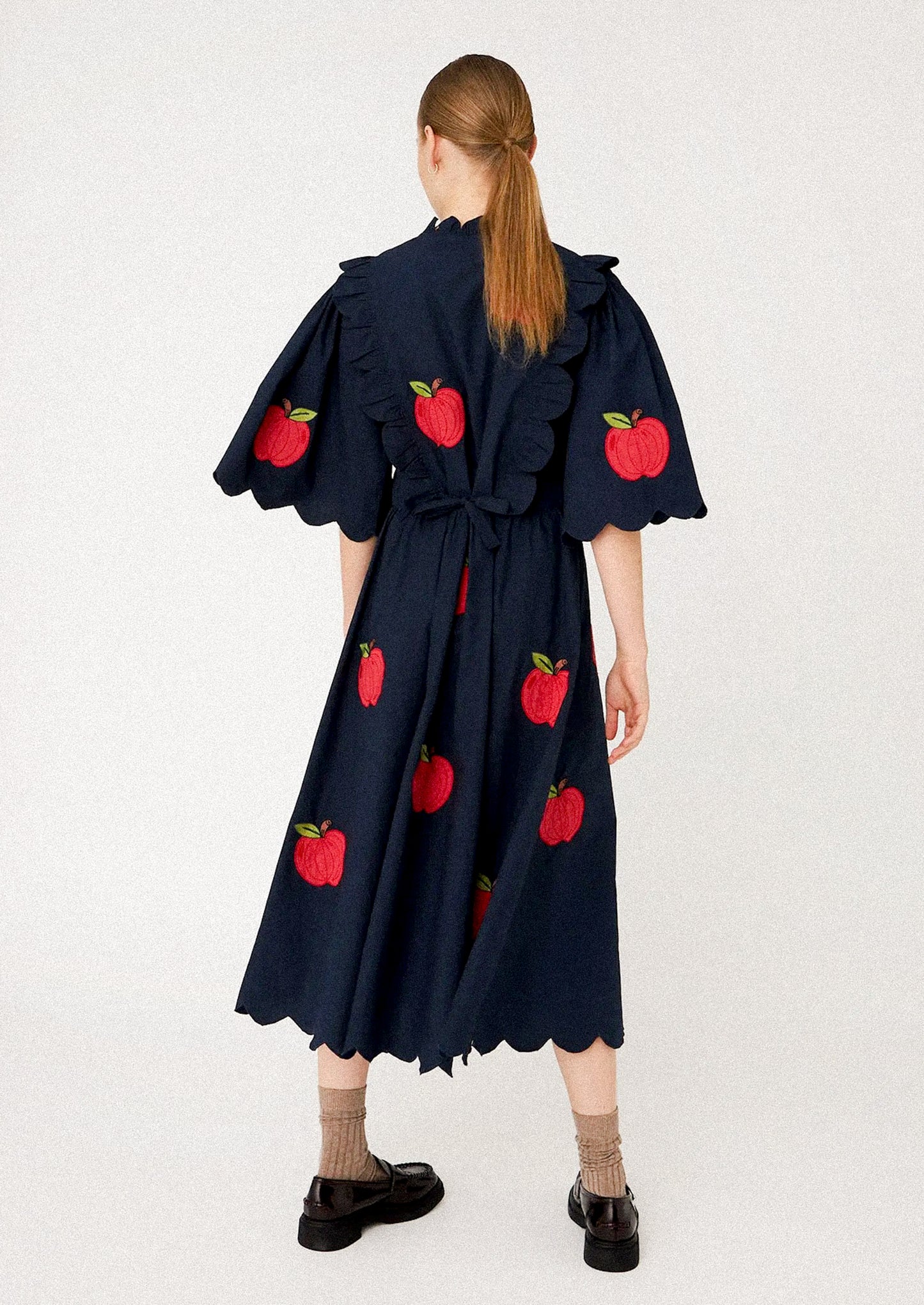 Woman wearing a navy dress with red apple patterns.