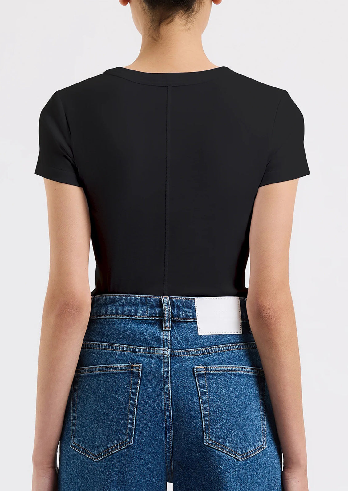 A person wearing a solid black fitted baby tee with tonal seam down back.
