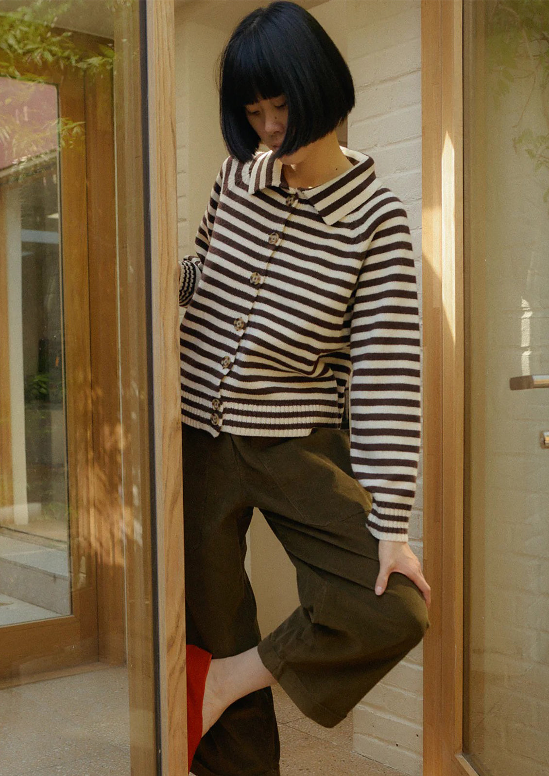 Person wearing a brown and white striped sweater in a room with wooden paneling.