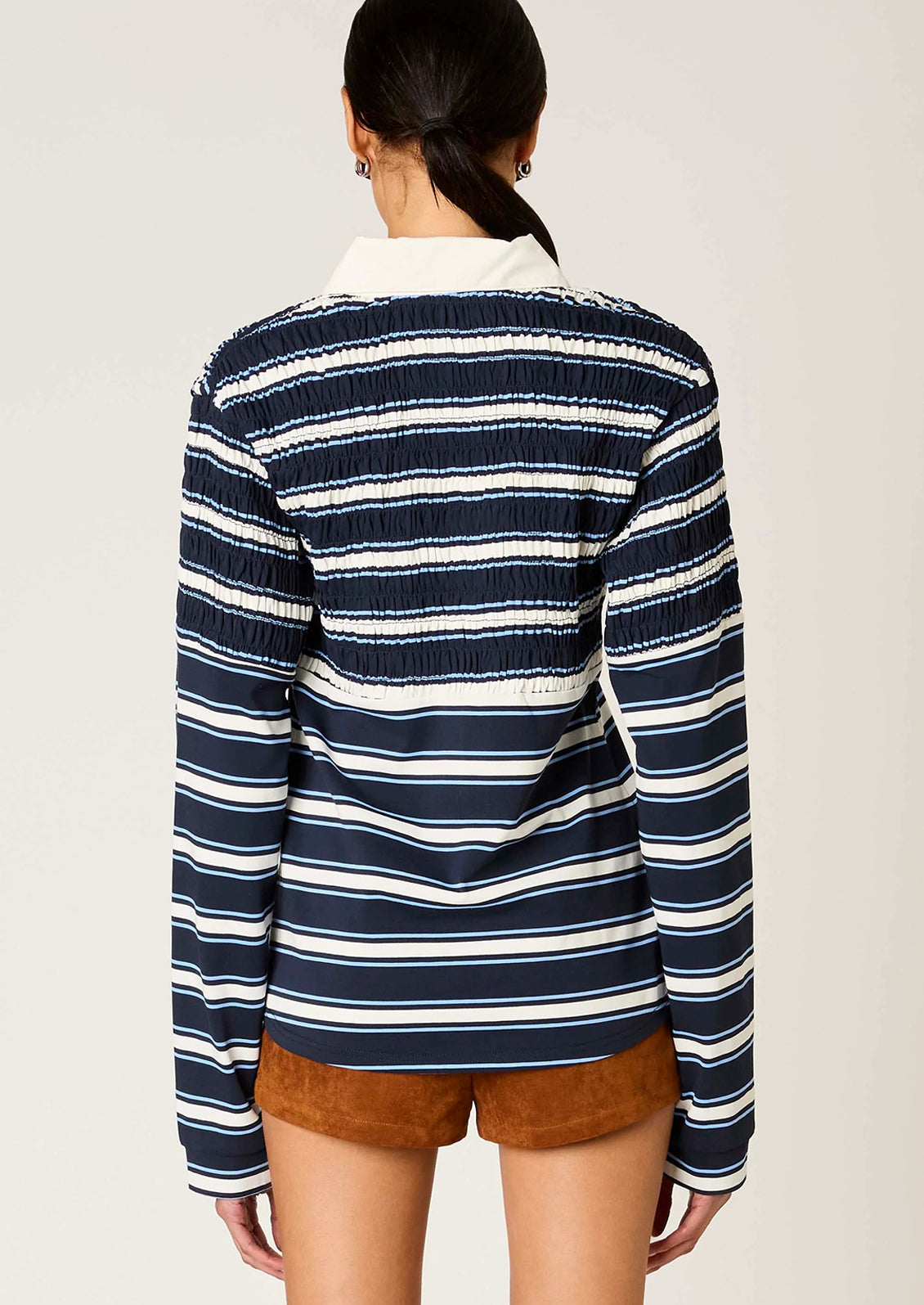 Person wearing a navy and white striped shirt with brown shorts on a plain background