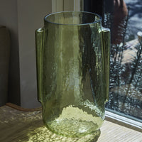 3: A transparent green glass vase in tall shape with side handle detail.