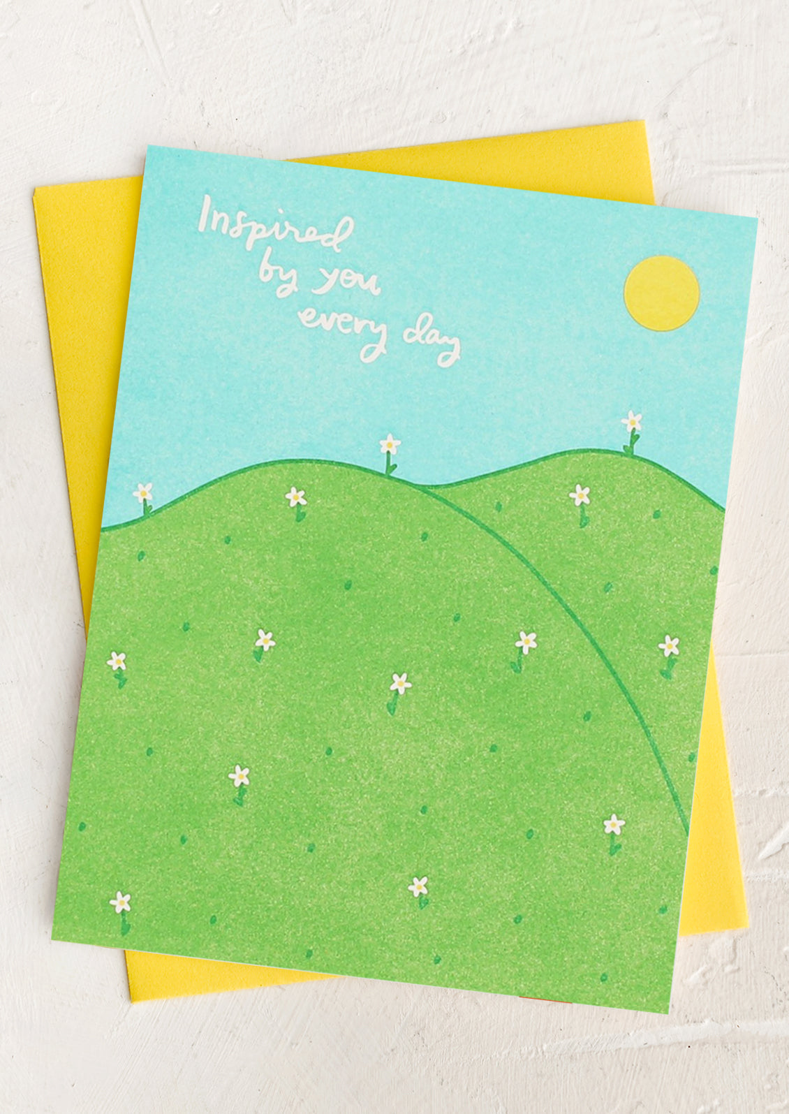 A card with illustration of hills and sun, text reads "Inspired by you every day".