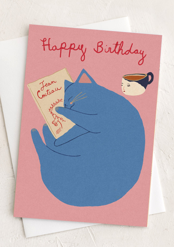 1: A pink greeting card with image of cat reading Jean Cocteau book.