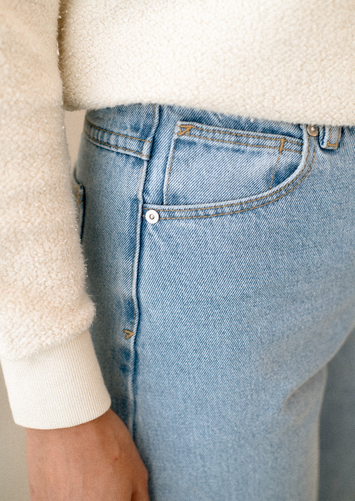 A woman wearing a pair of blue jeans with high rise and wide leg.