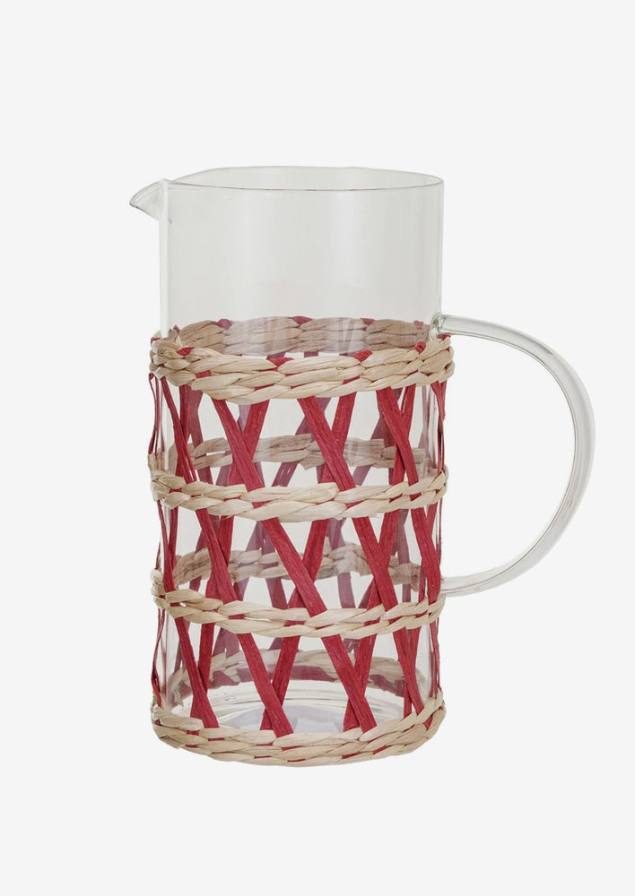 A clear glass pitcher with red and natural rattan sheath.