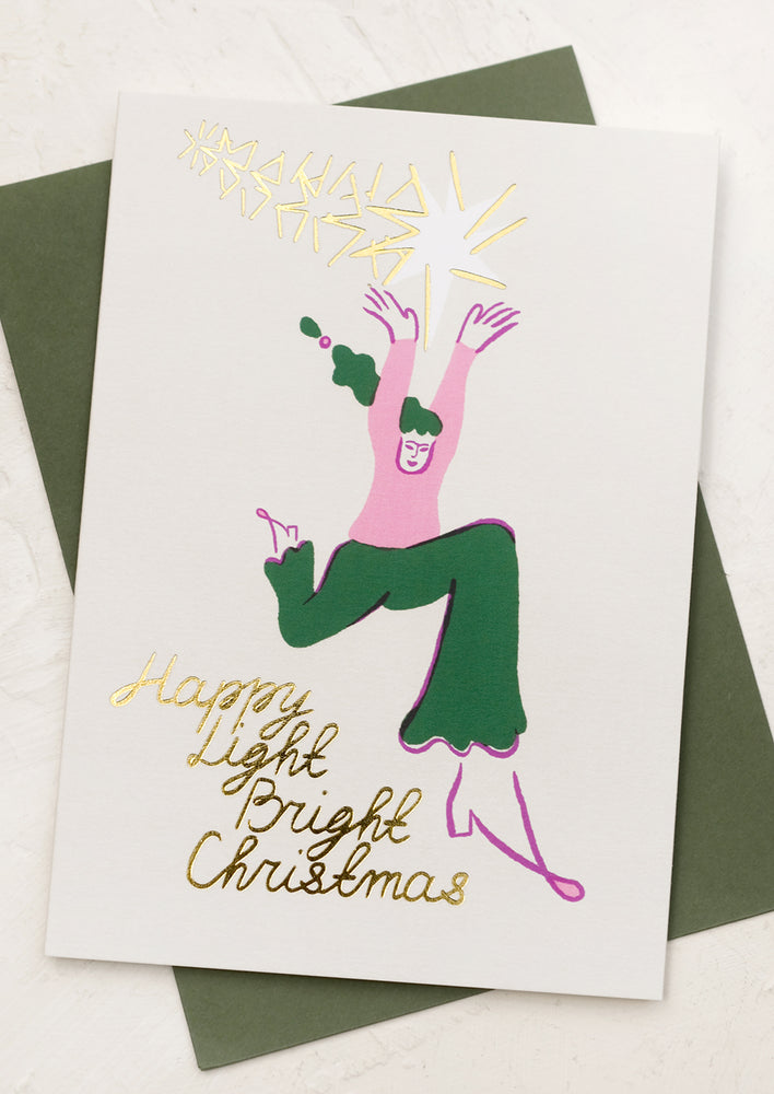 A card with illustration of woman jumping with stars, text reads "Happy Light Bright Christmas".