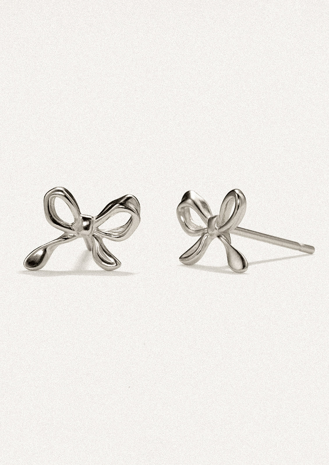 A pair of small stud earrings in silver, in the shape of a small bow.