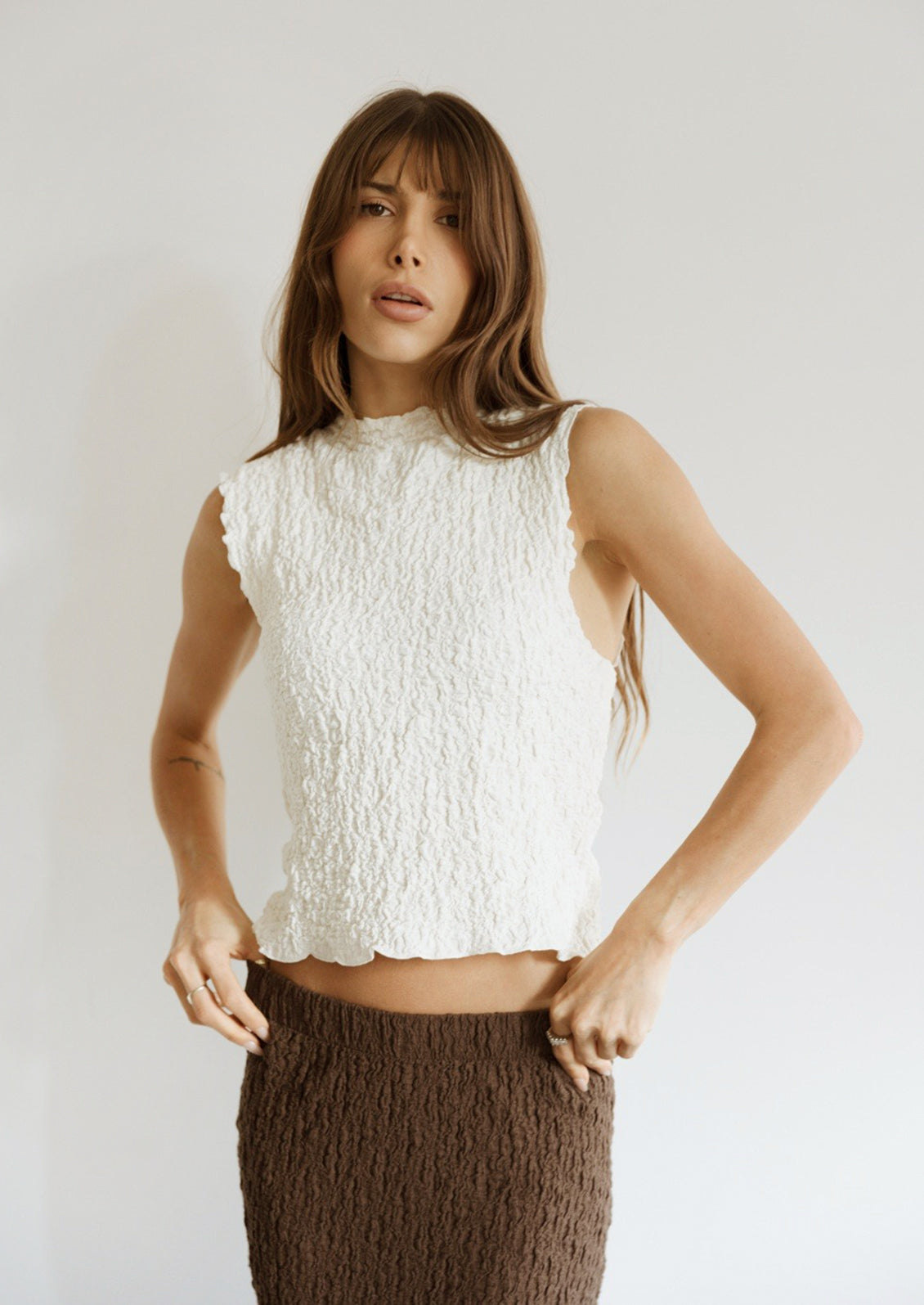 A woman wearing a sleeveless cream top with crinkled texture.
