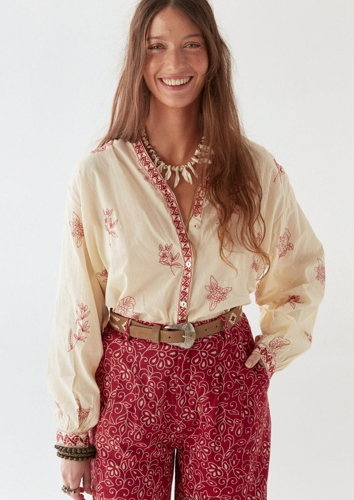 A person wearing a cream colored blouse with red floral embroidery.