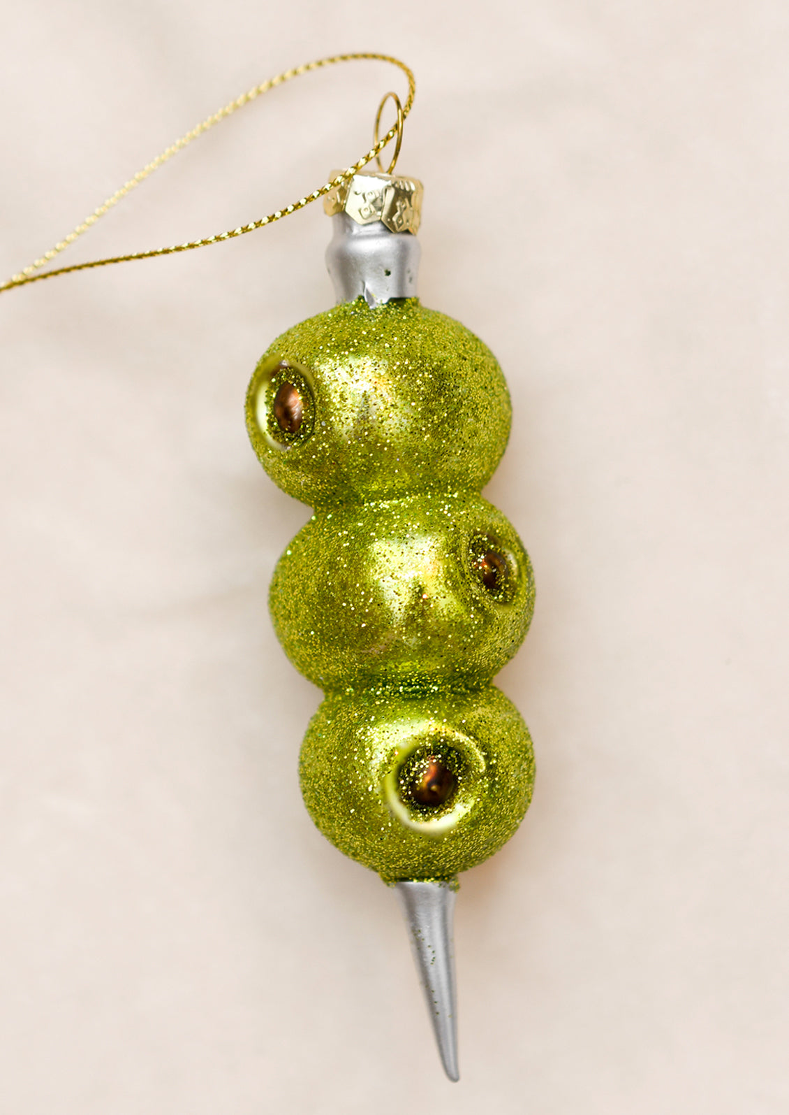 A glass ornament of three pimento olives on a martini skewer.