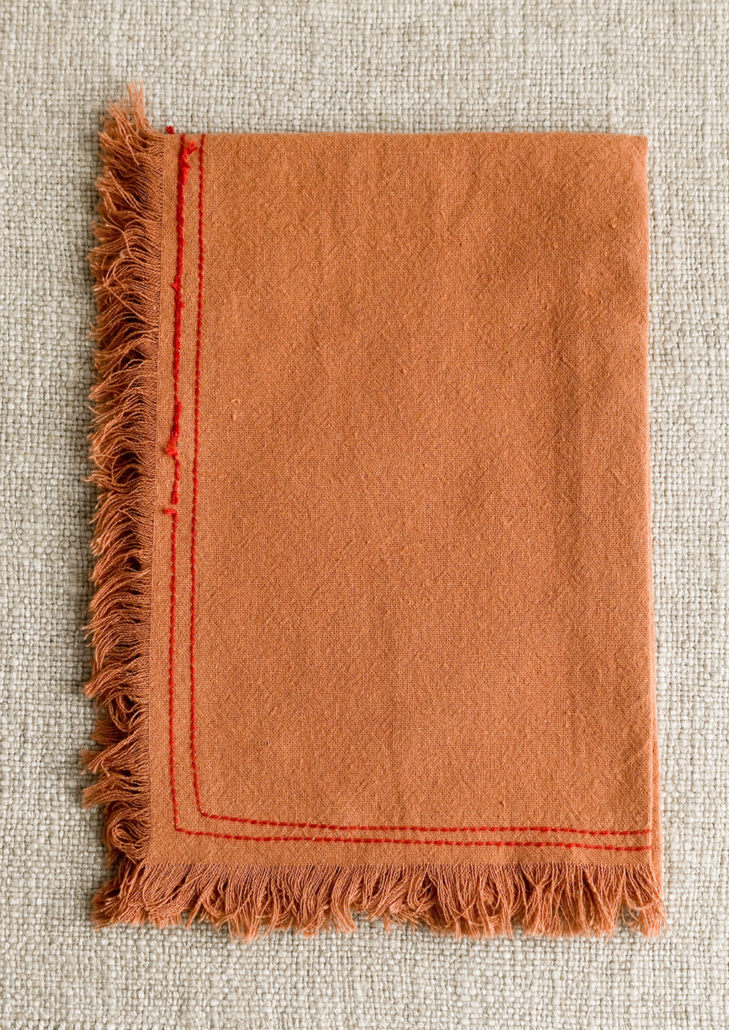 Annatto: An orange tea towel with red stitching.