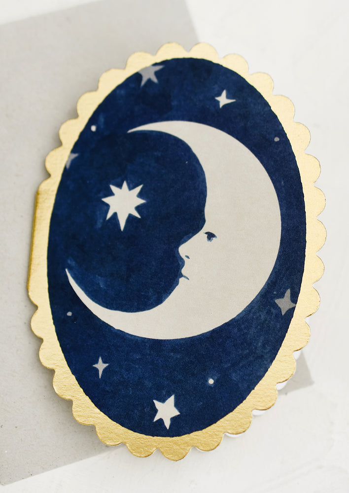 An oval shaped card with moon print and scalloped edges.