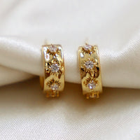 1: A pair of small gold hoop earrings with raised crystal starbust pattern.