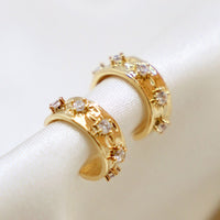 2: A pair of small gold hoop earrings with raised crystal starbust pattern.