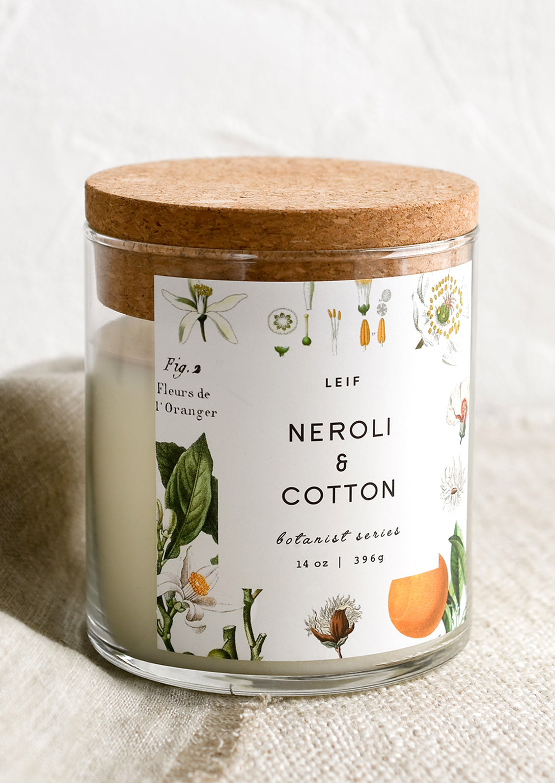 A glass candle with a cork lid and white botanical printed label reading "neroli and cotton".