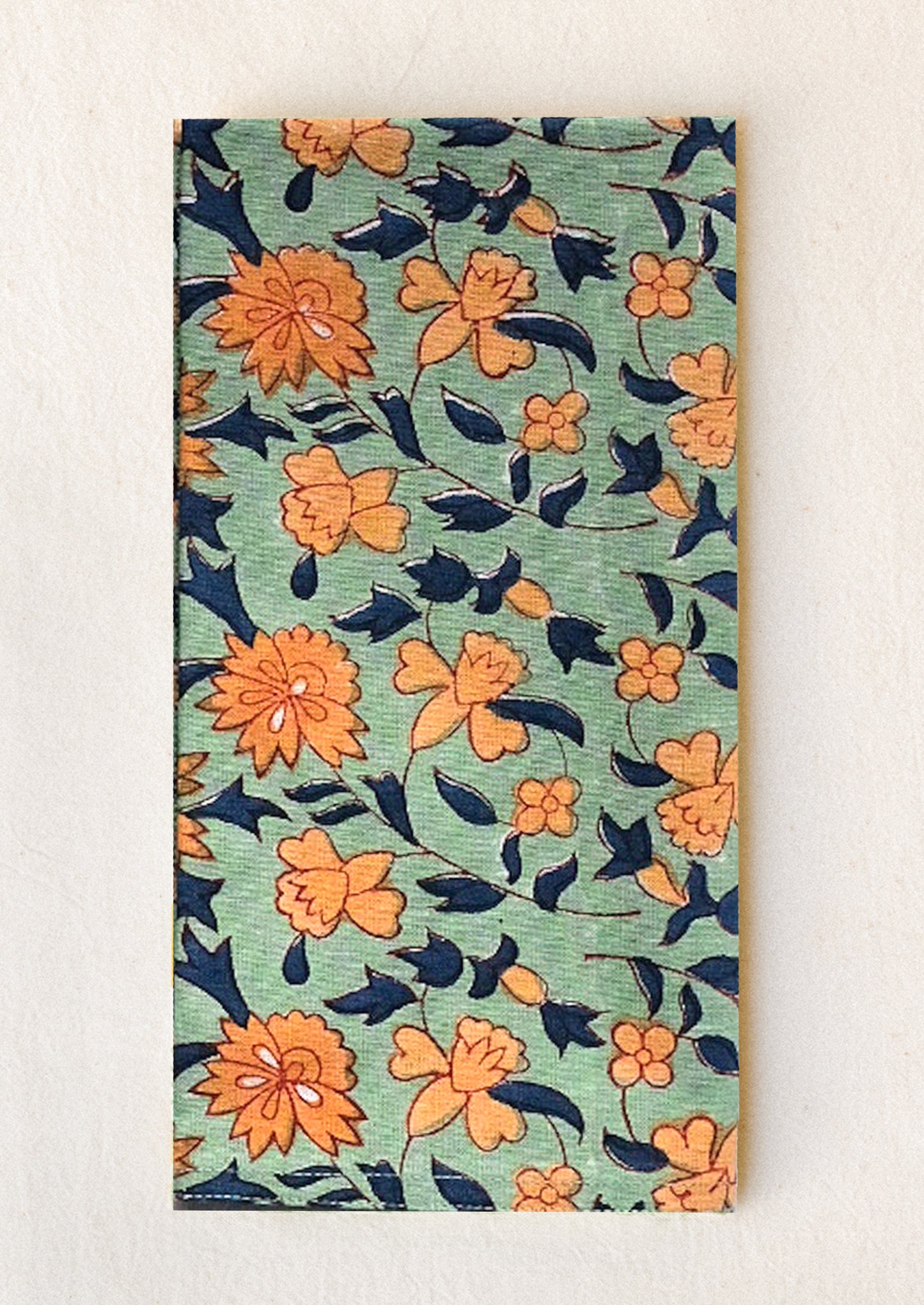A cotton napkin in sage green with orange and navy floral print.