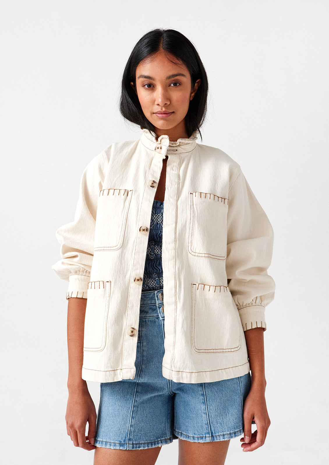 Woman wearing an ecru, cotton jacket and denim shorts.